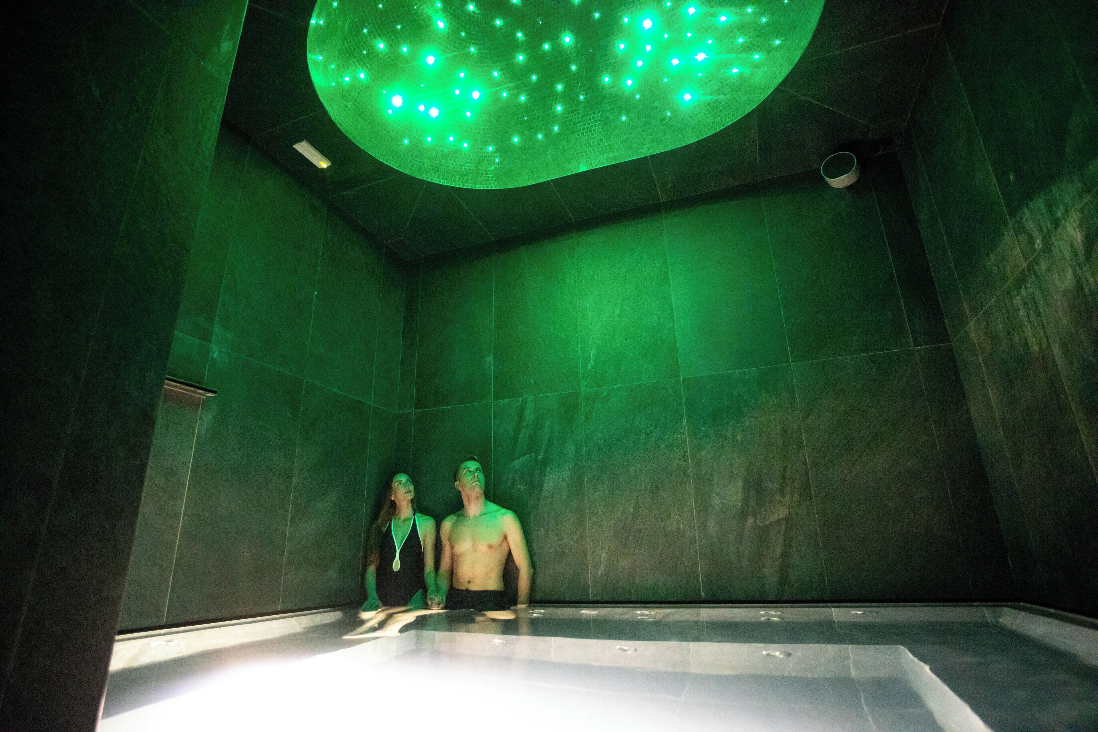 A room with a large, empty bathtub and a ceiling with green lights.