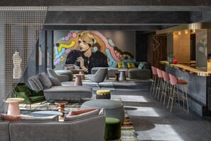 Un espace de détente moderne, doté de canapés, de fauteuils, d’un bar et d’une fresque murale aux couleurs vives.