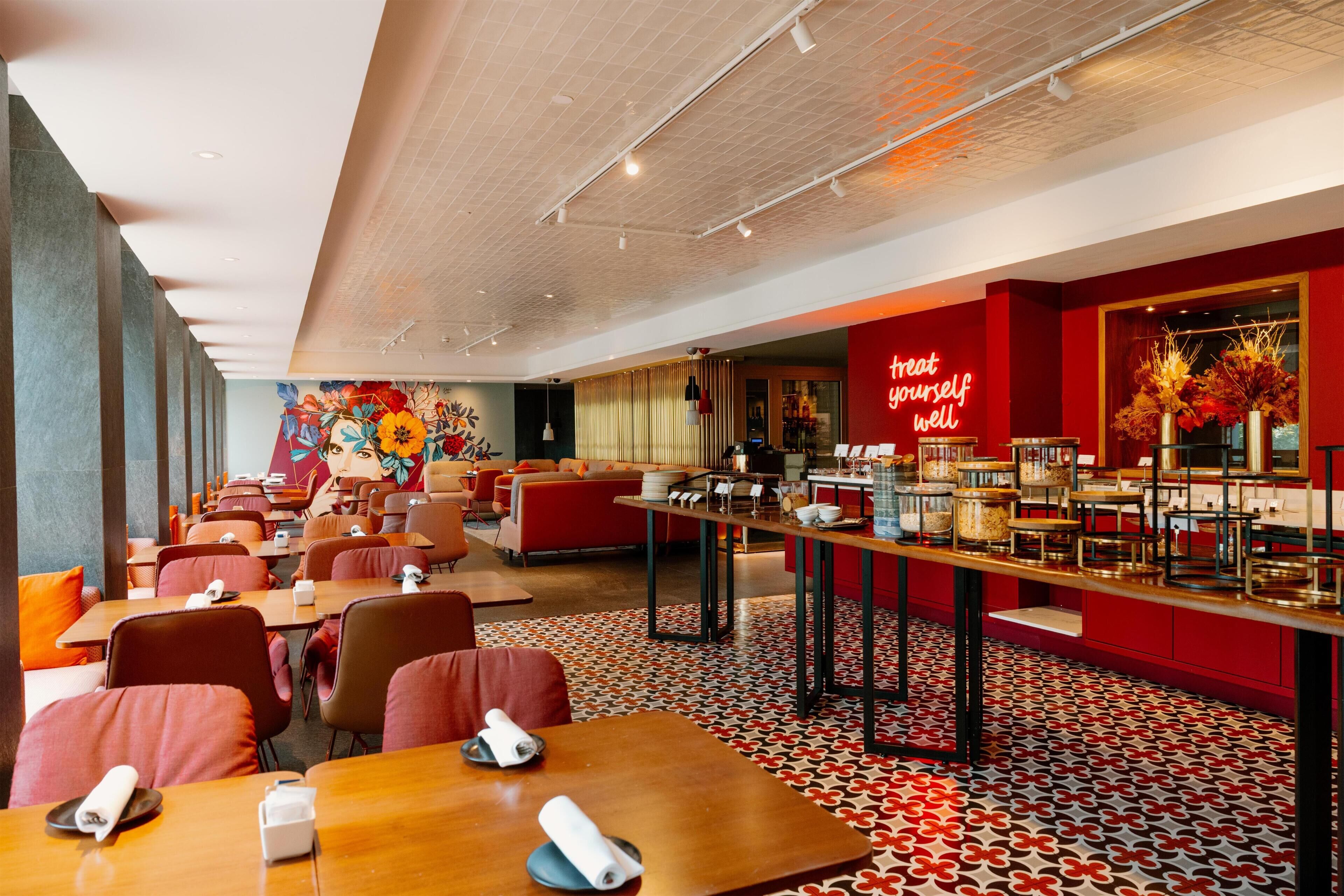 Un restaurante moderno con una barra larga, zona de mesas y un mural vibrante.