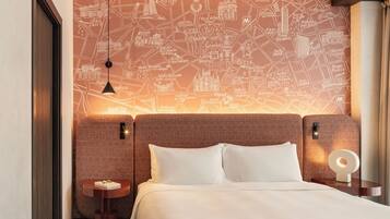 Hotelkamer met stadsgezicht aan de muur, een bed met witte lakens, twee nachtkastjes en een hanglamp.