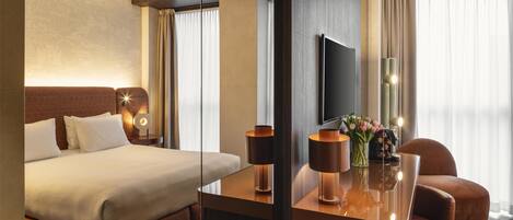 Une chambre d’hôtel avec un lit, un bureau avec une lampe, une chaise, une télévision et une fenêtre avec des rideaux.