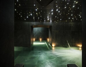 Et dæmpet oplyst, moderne spa med et centralt vandelement og et loft pyntet med små lys.
