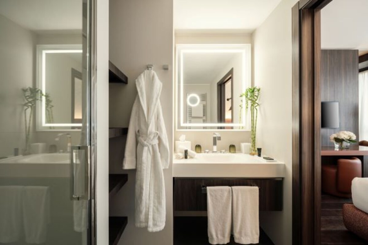 Un baño moderno con cabina de ducha de vidrio, un espejo grande con iluminación integrada, un lavabo blanco y un mueble de tocador de madera oscura.