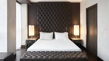 A hotel room with a large bed, two bedside lamps, a dark headboard, and a wooden bench.