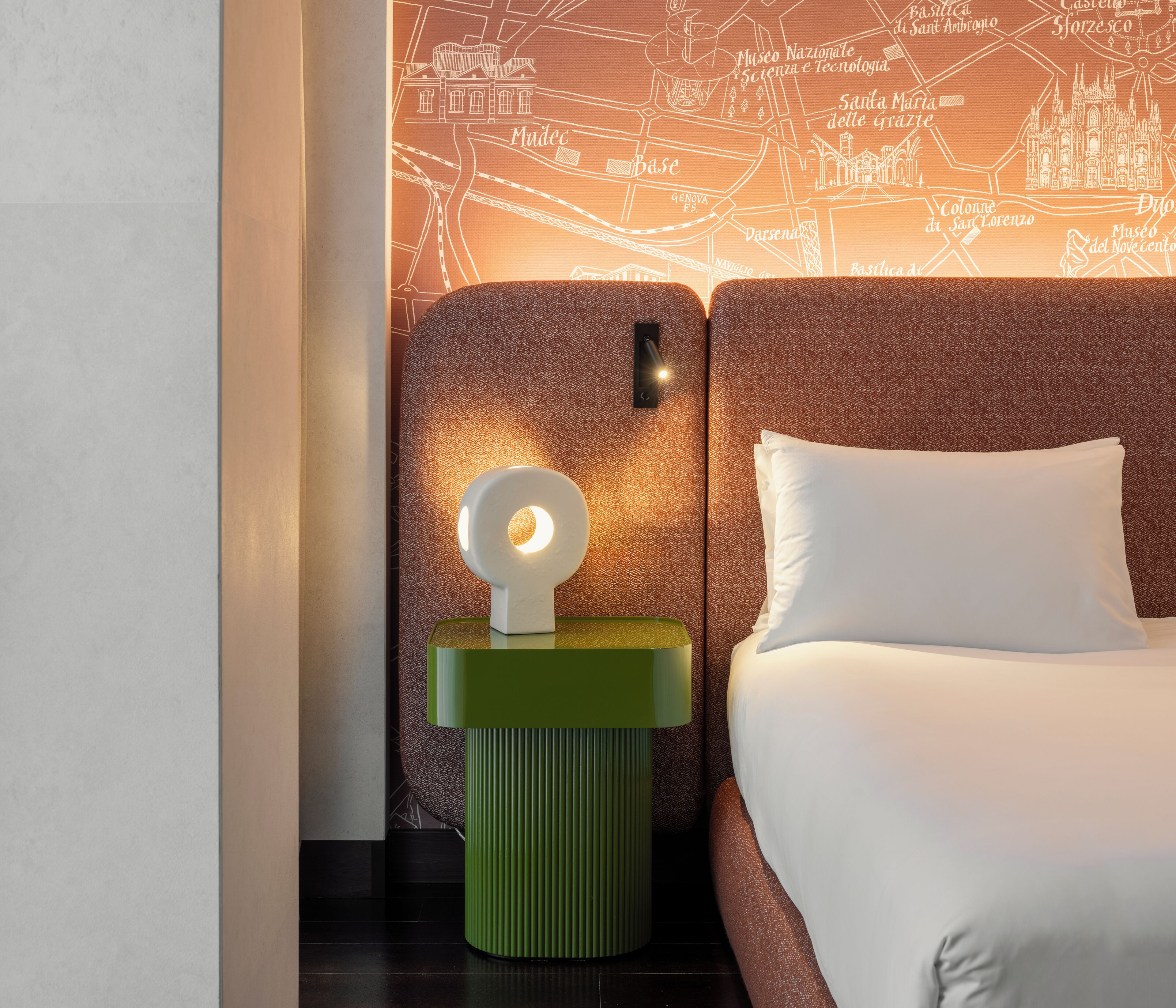 Een hotelkamer met een bed, een groen nachtkastje met een lamp, en een wereldkaart aan de muur.
