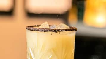 Een hand strooit een substantie over een glas met een patroon, geplaatst op een oppervlak met een raster.
