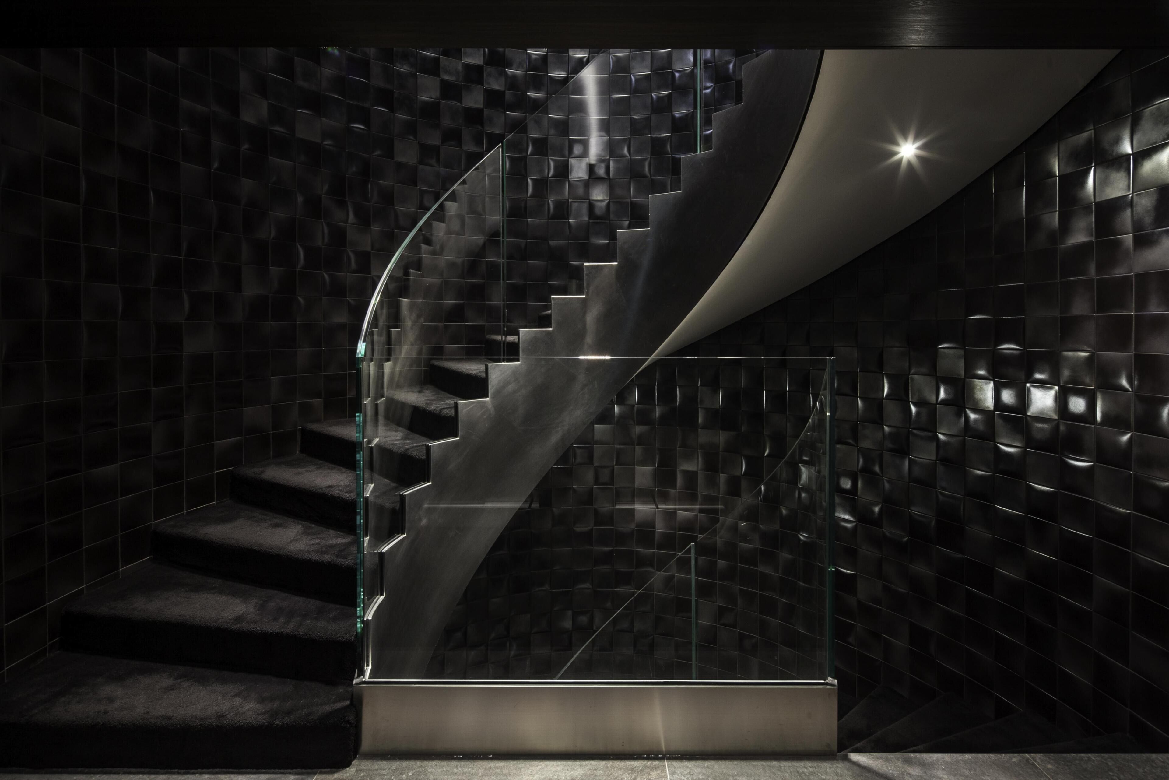 A modern staircase with a glass railing, surrounded by dark, textured walls.