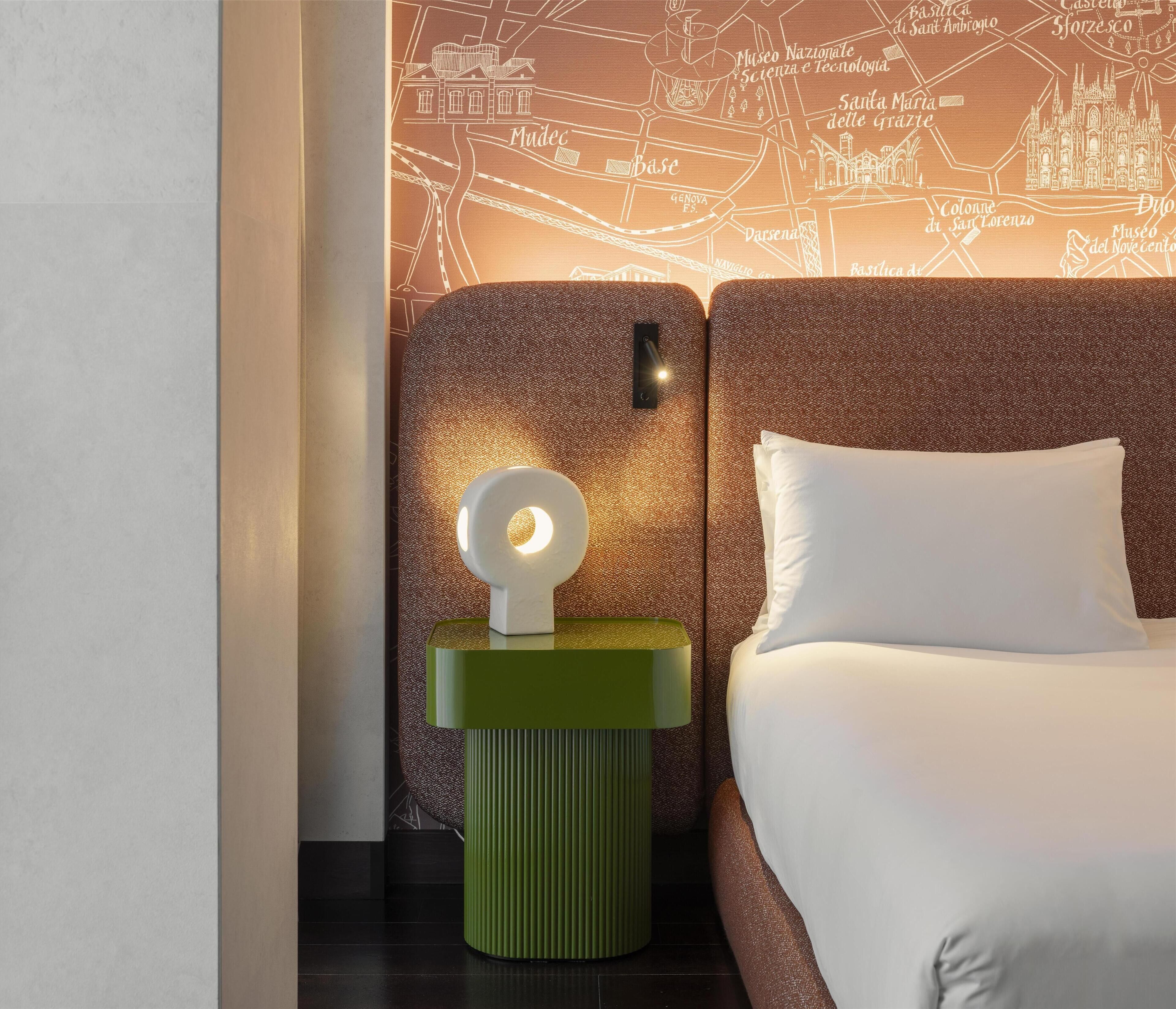 Una habitación de hotel con una cama, una mesita de noche con una lámpara y una pared con un mapa.