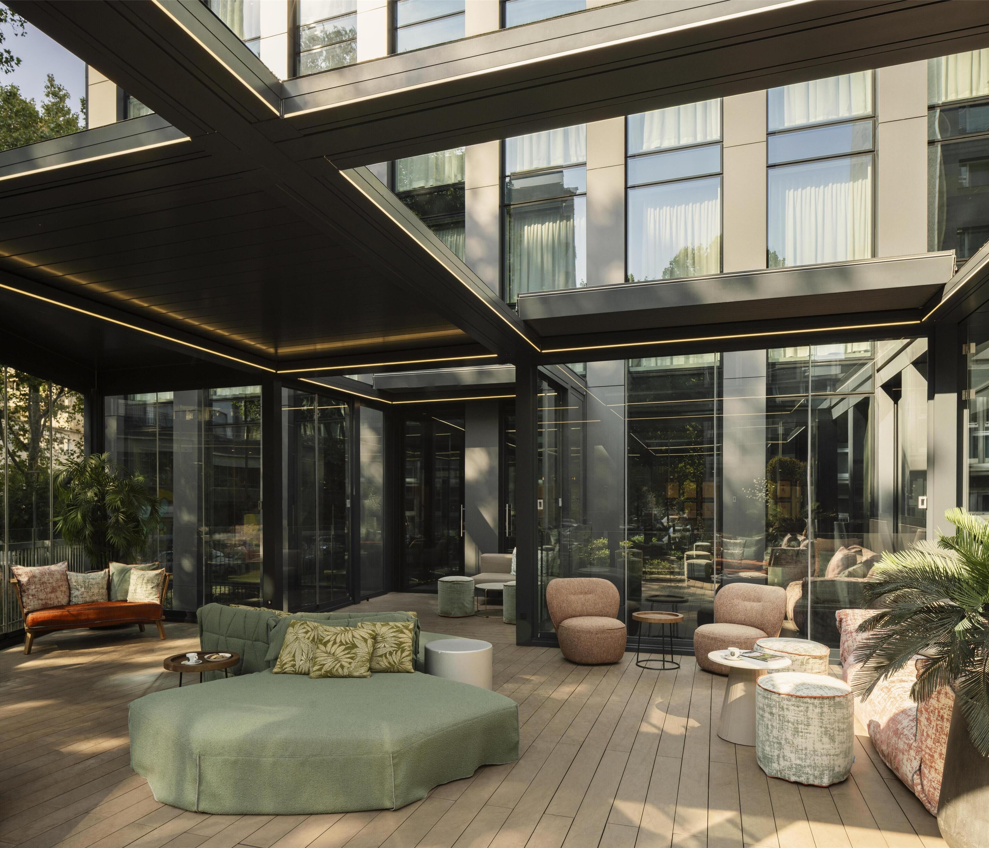A modern outdoor lounge area with seating, glass walls, and a wooden deck.
