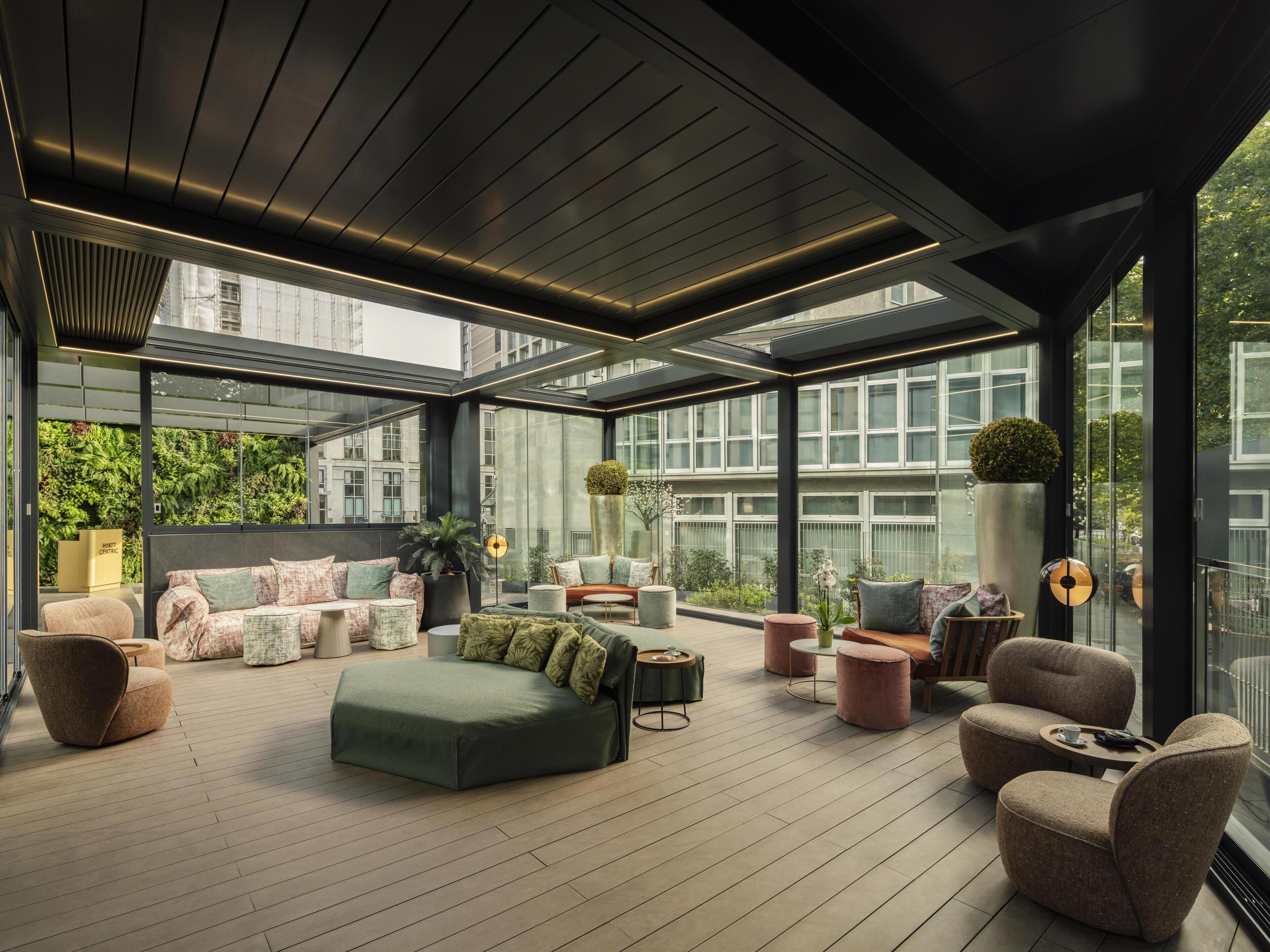 A modern, open-plan living area with a variety of seating options, a large window offering a view of the cityscape, and a ceiling with integrated lighting.