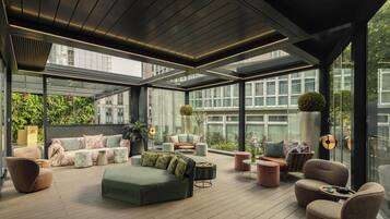 A modern, open-plan living area with a variety of seating options, a large window offering a view of the cityscape, and a ceiling with integrated lighting.