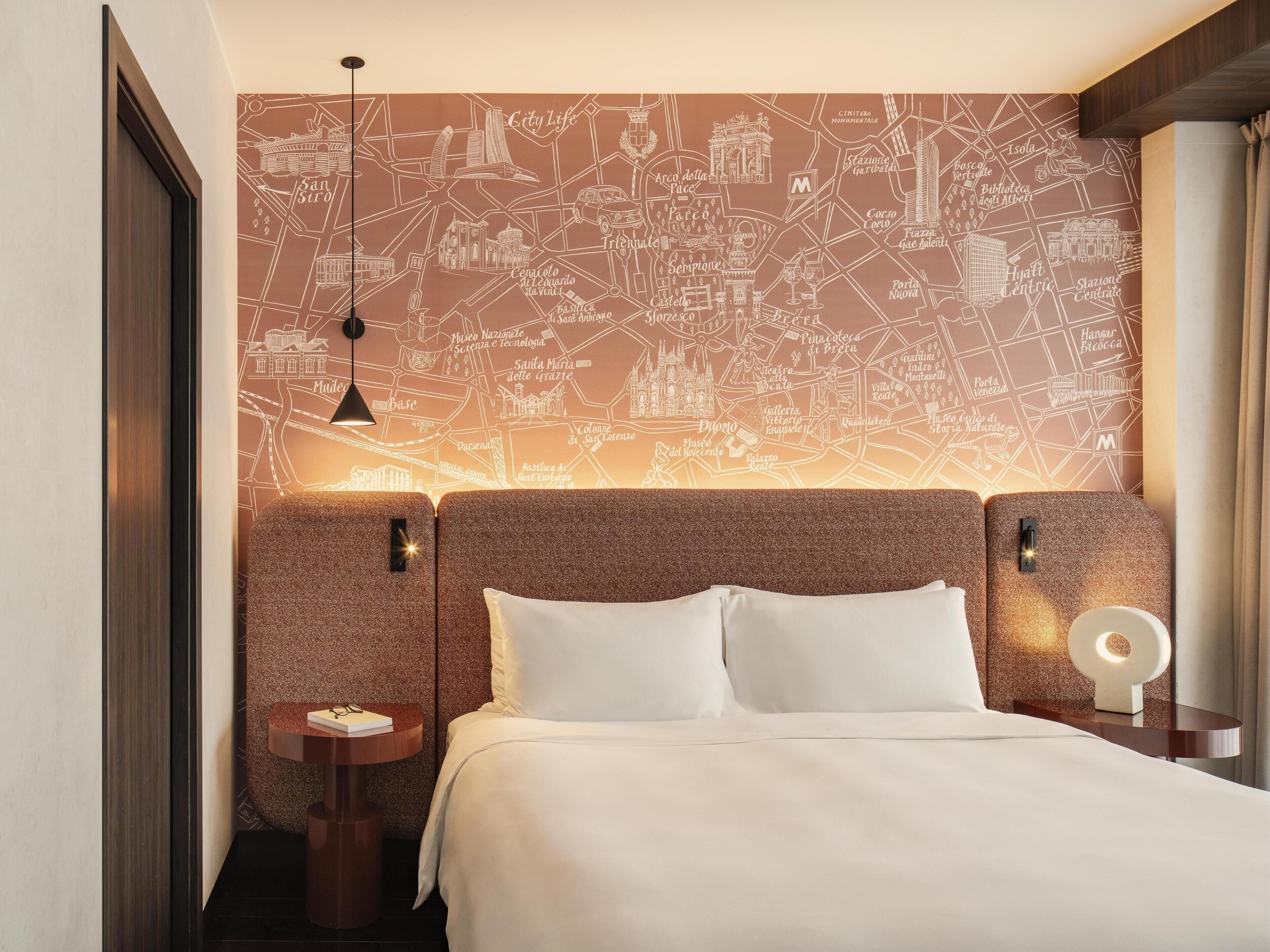 A hotel room with a large bed, two bedside tables, a wall map, and a hanging light fixture.