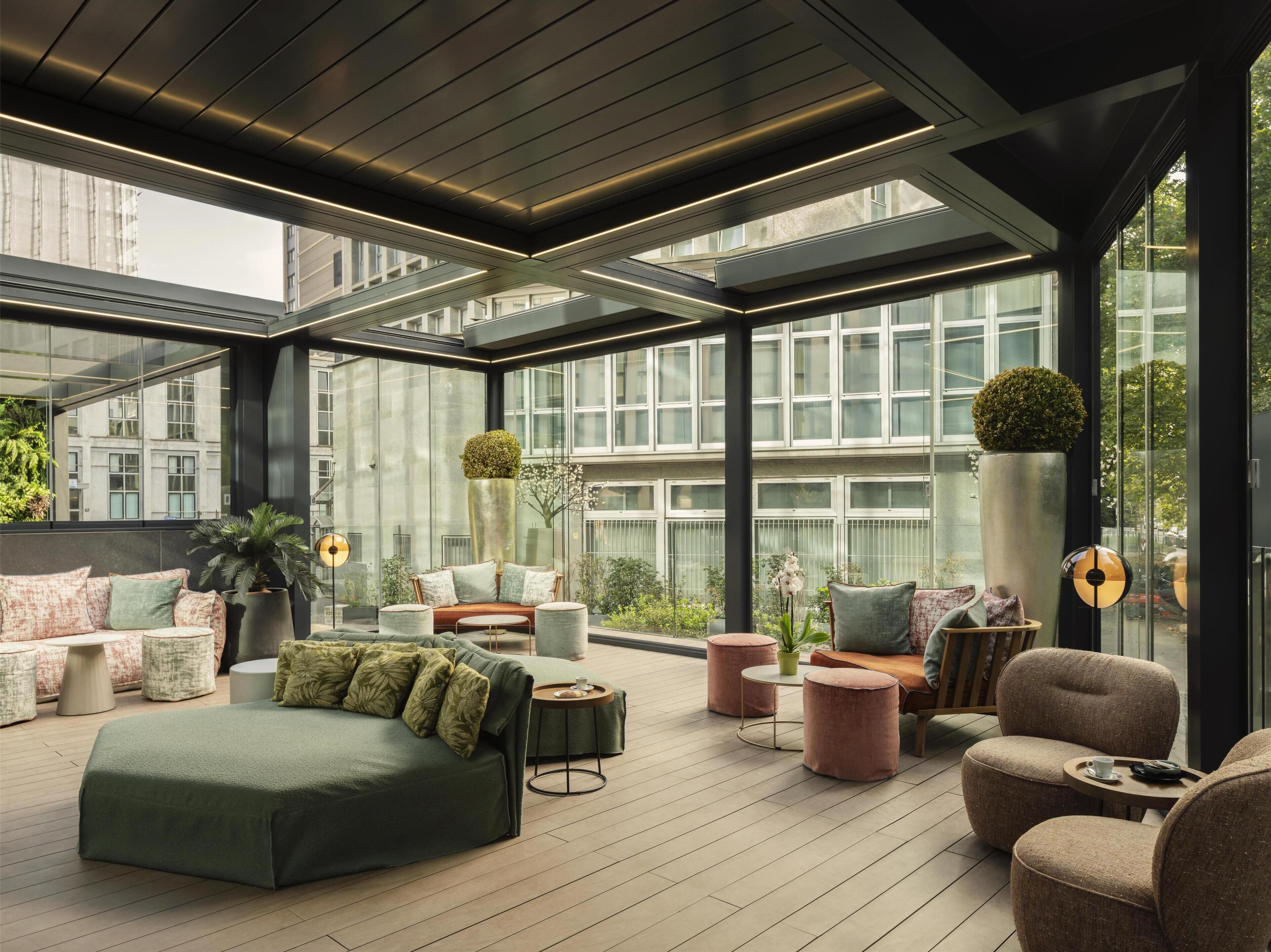 A modern rooftop lounge with a glass ceiling, comfortable seating, and a view of the cityscape.