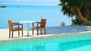 Una piscina con vistas al mar, dos sillas de mimbre y una mesita.