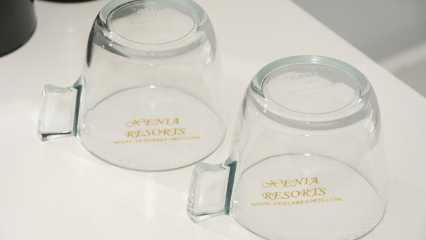 Two clear glass mugs with handles, each labeled 'XENIA RESORTS' and a website address. - Porto Evia Boutique Hotel by Xenia Resorts (Eretria)