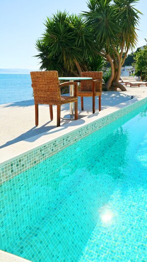 A poolside area with a tiled edge, two wicker chairs, and a table. - Porto Evia Boutique Hotel by Xenia Resorts (Eretria)