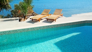 A clear blue pool with tiled edges, two lounge chairs, and a palm tree. - Porto Evia Boutique Hotel by Xenia Resorts (Eretria)