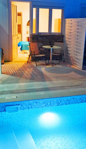 A swimming pool with a tiled edge, a patio area with a table and chairs, and a stone wall. - Porto Evia Boutique Hotel by Xenia Resorts (Eretria)