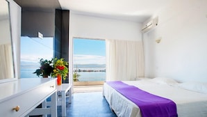 Habitación de hotel con cama, escritorio, silla, ventana con vista al mar y planta en maceta.