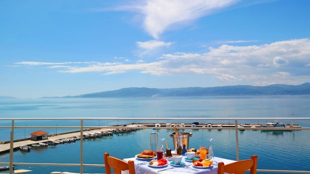 Una mesa de comedor con comida y bebidas, vista al mar y una costa lejana.