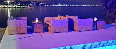 Un área junto a la piscina con mobiliario de mimbre y una piscina con baldosas.
