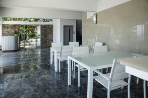 A modern dining area with glass tables and chairs, a stone wall, and a door leading outside. - Porto Evia Boutique Hotel by Xenia Resorts (Eretria)