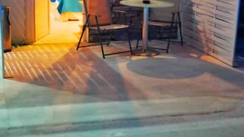 Una piscina con borde de azulejos, un patio con mesa y sillas, y una pared de piedra.