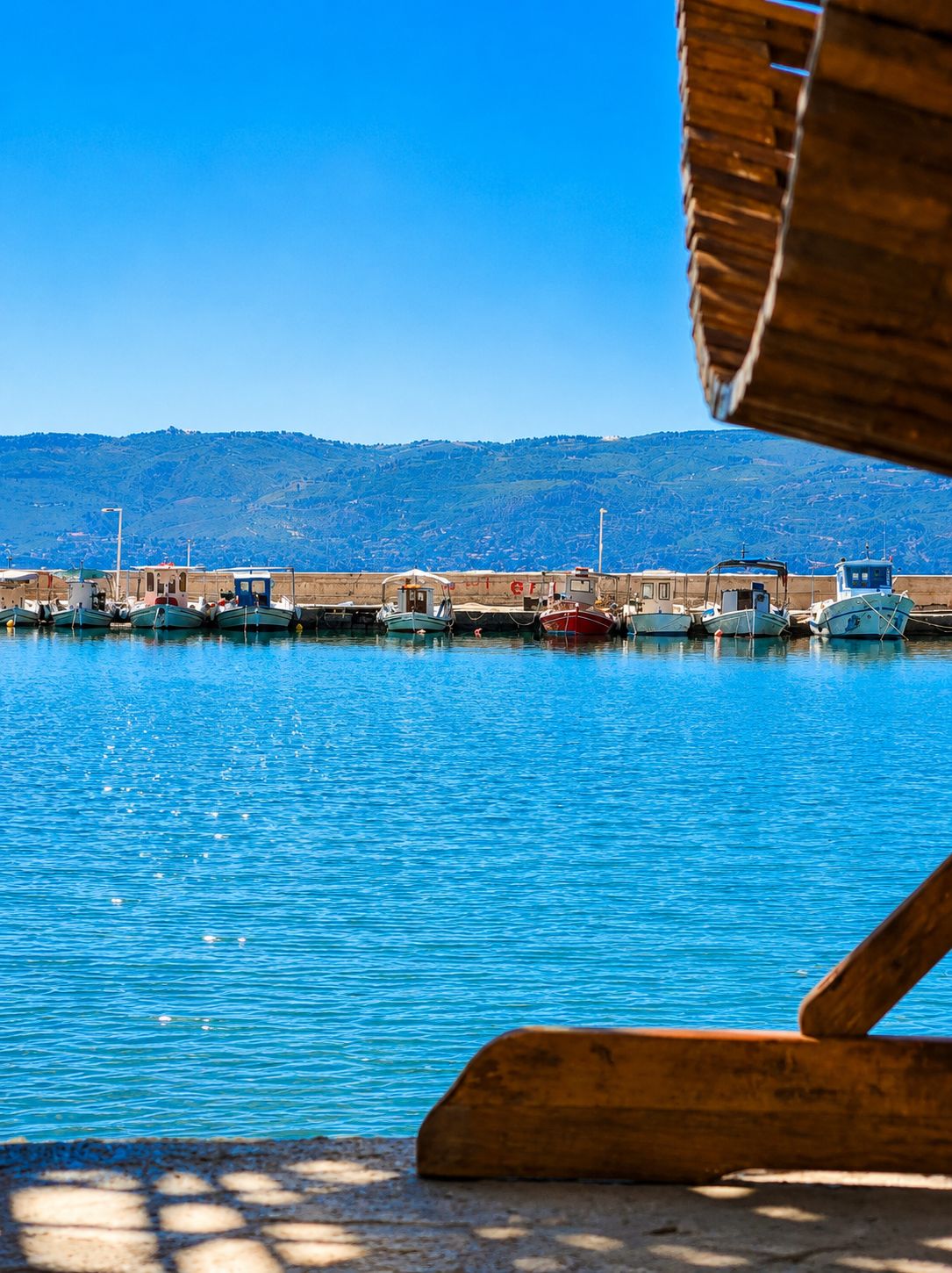 Un puerto con barcos amarrados, un cielo azul despejado y un paisaje montañoso al fondo.