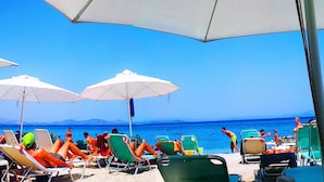 Una playa con filas de tumbonas y sombrillas, un cielo azul despejado y el mar al fondo.