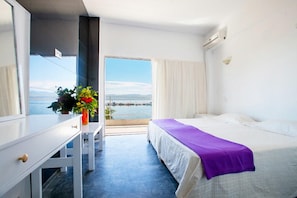 A hotel room with a bed, a desk, a chair, a window with a view of the sea, and a potted plant. - Porto Evia Boutique Hotel by Xenia Resorts (Eretria)