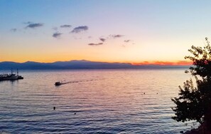 A calm lake at sunset with boats and a distant mountain range.