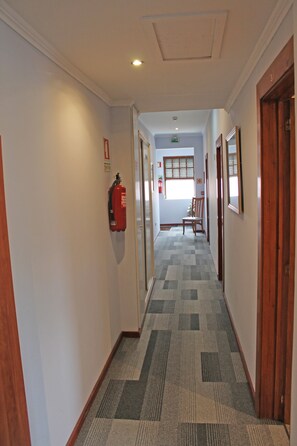 A hallway with patterned carpet, wooden doors, and a fire extinguisher mounted on the wall. - Residencial Paranhos (Porto)