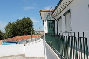 A white building with a green balcony railing, a tiled roof, and a clear sky. - Residencial Paranhos (Porto)