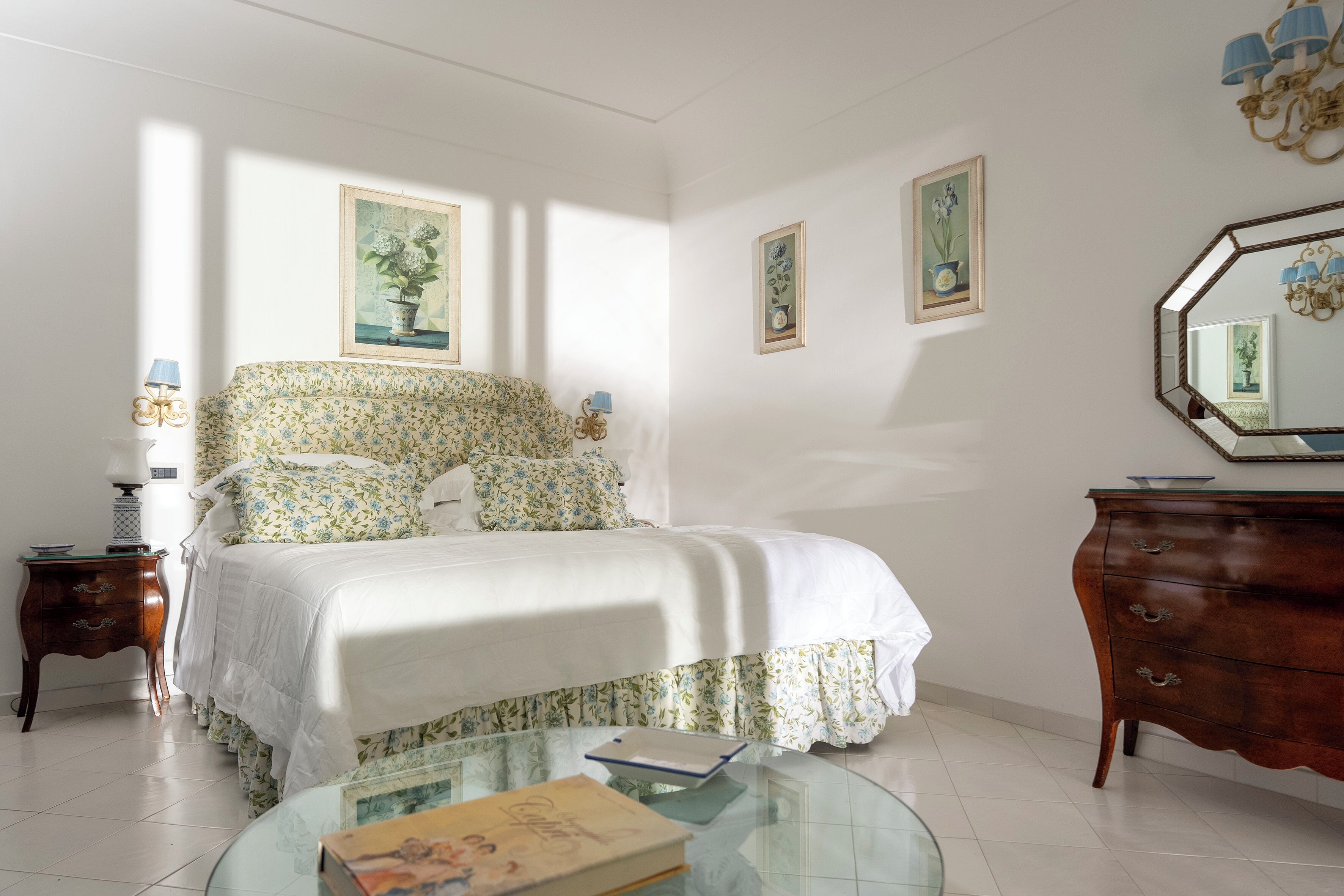 A bedroom with a bed, a dresser, a nightstand, and a glass table with books.