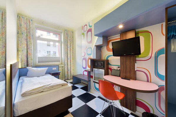 Een hotelkamer met een bed, een bureau met stoel, een televisie en een raam met gordijnen.