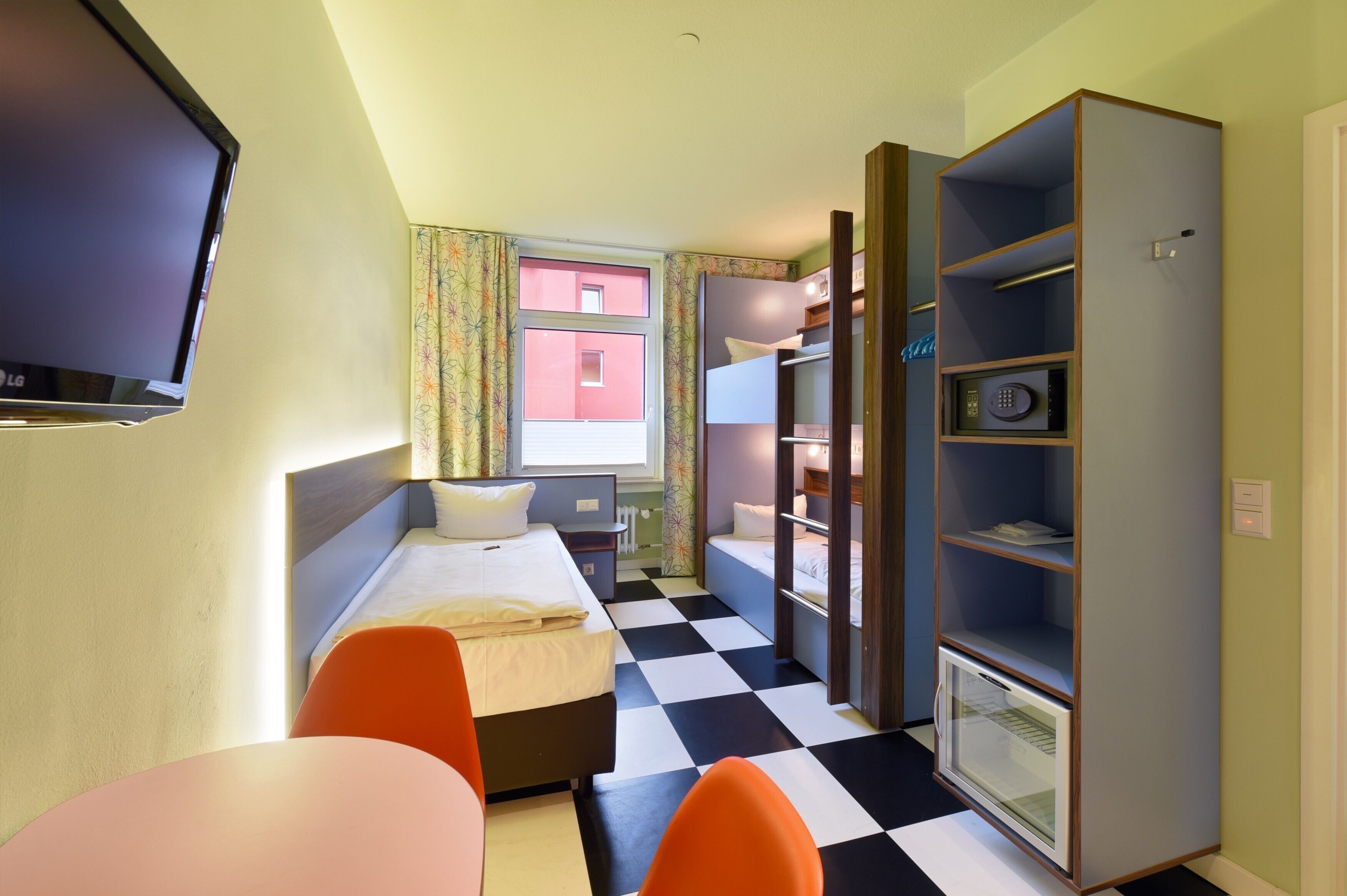 Una habitación de hotel pequeña con cama, escritorio, silla, televisión y armario.