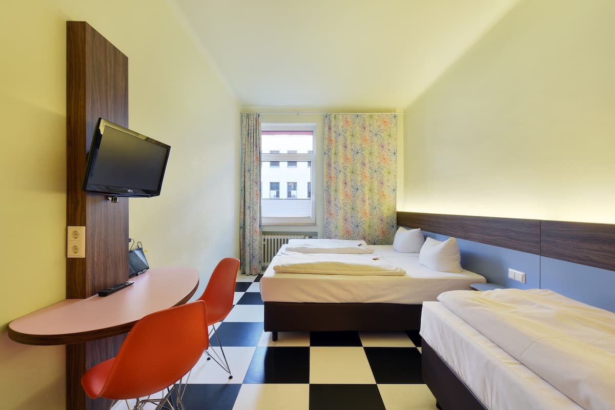 Een hotelkamer met een bed, een bureau met stoel, een televisie en een raam met gordijnen.