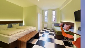Ein Hotelzimmer mit zwei Betten, einem Sofa, einem Esstisch und einem Fernseher.