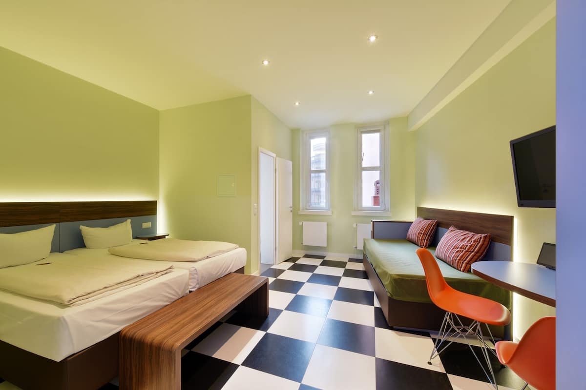 Een hotelkamer met twee bedden, een slaapbank, een eettafel en een televisie.