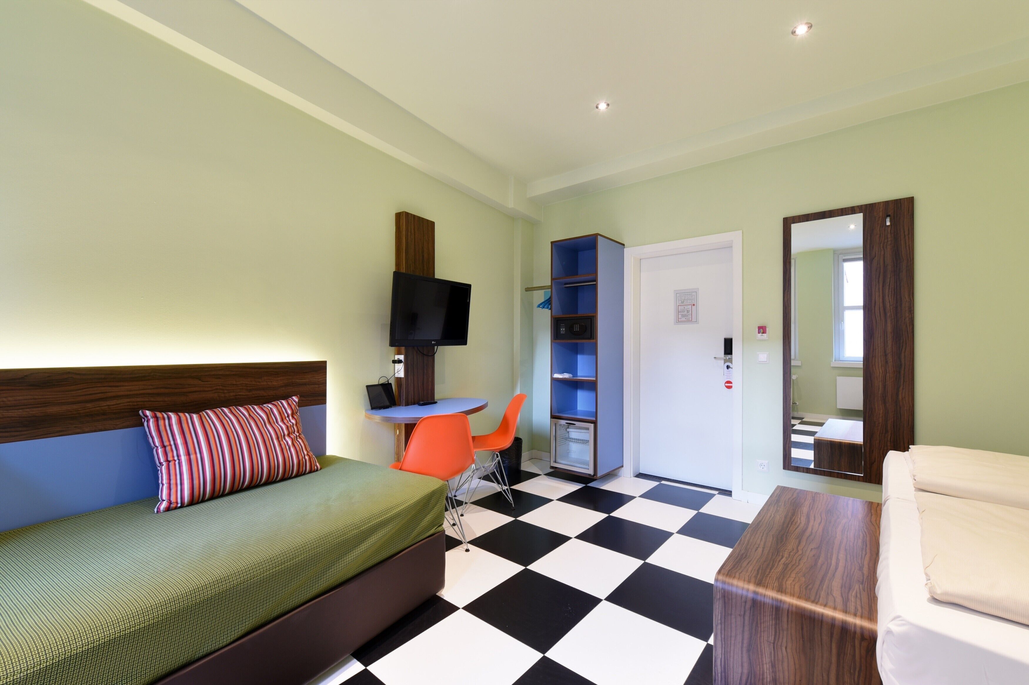 Una habitación con cama, escritorio, televisor y armario.