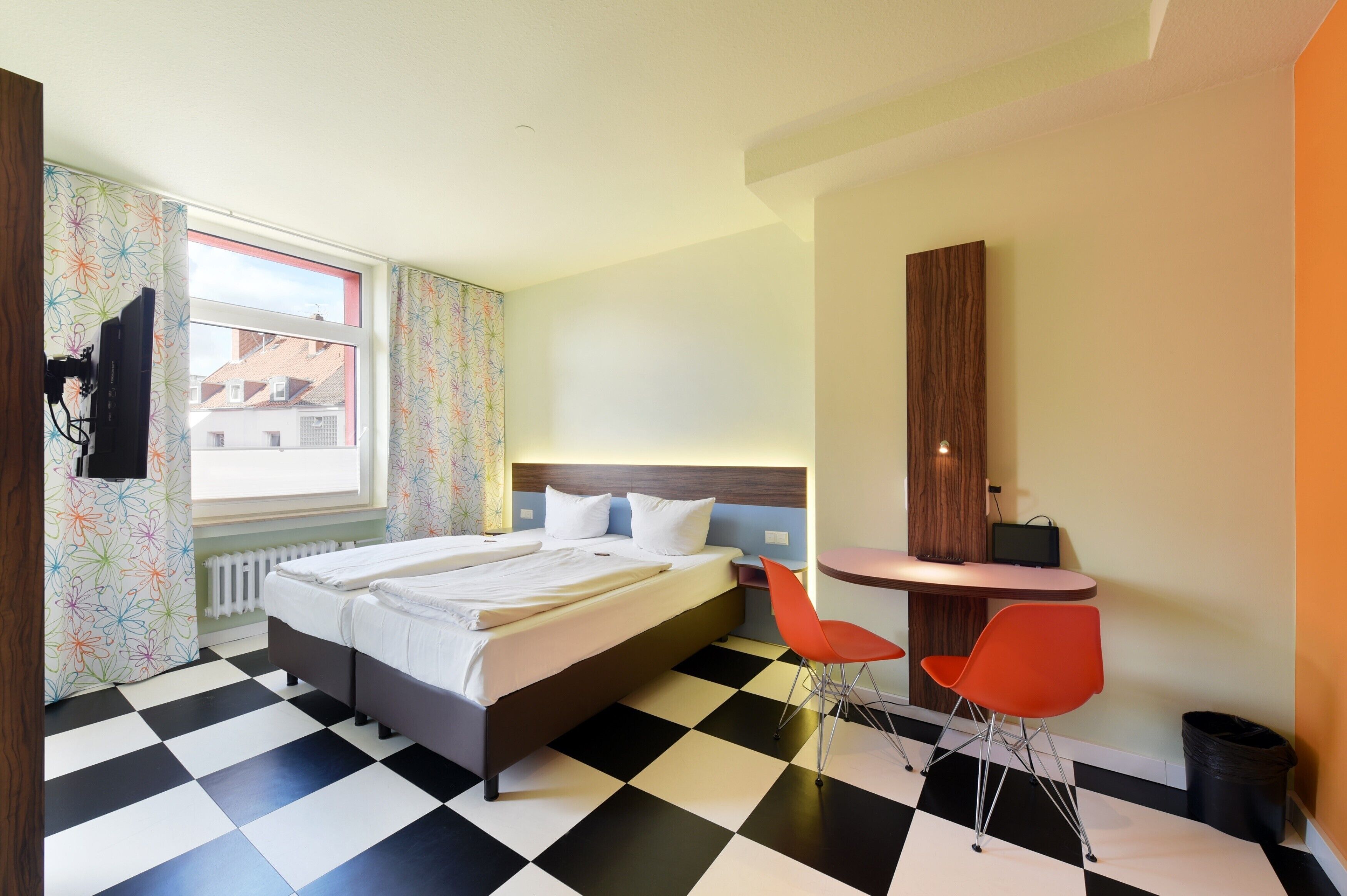 A hotel room with a bed, two red chairs, a desk, and a window with curtains.