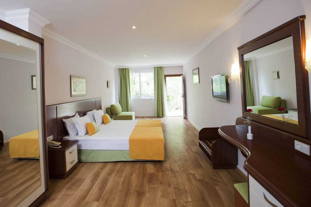Habitación de hotel con cama, mesita de noche, silla y un espejo grande.