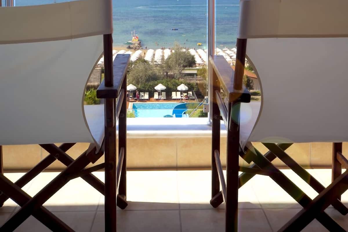 Un balcón con dos sillas blancas que dan a una piscina y al mar.