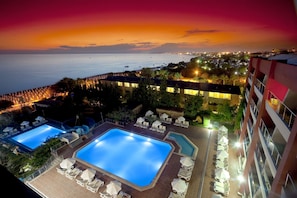 Un hôtel doté de deux piscines, d’un espace extérieur aménagé et offrant une vue sur la mer au coucher du soleil.