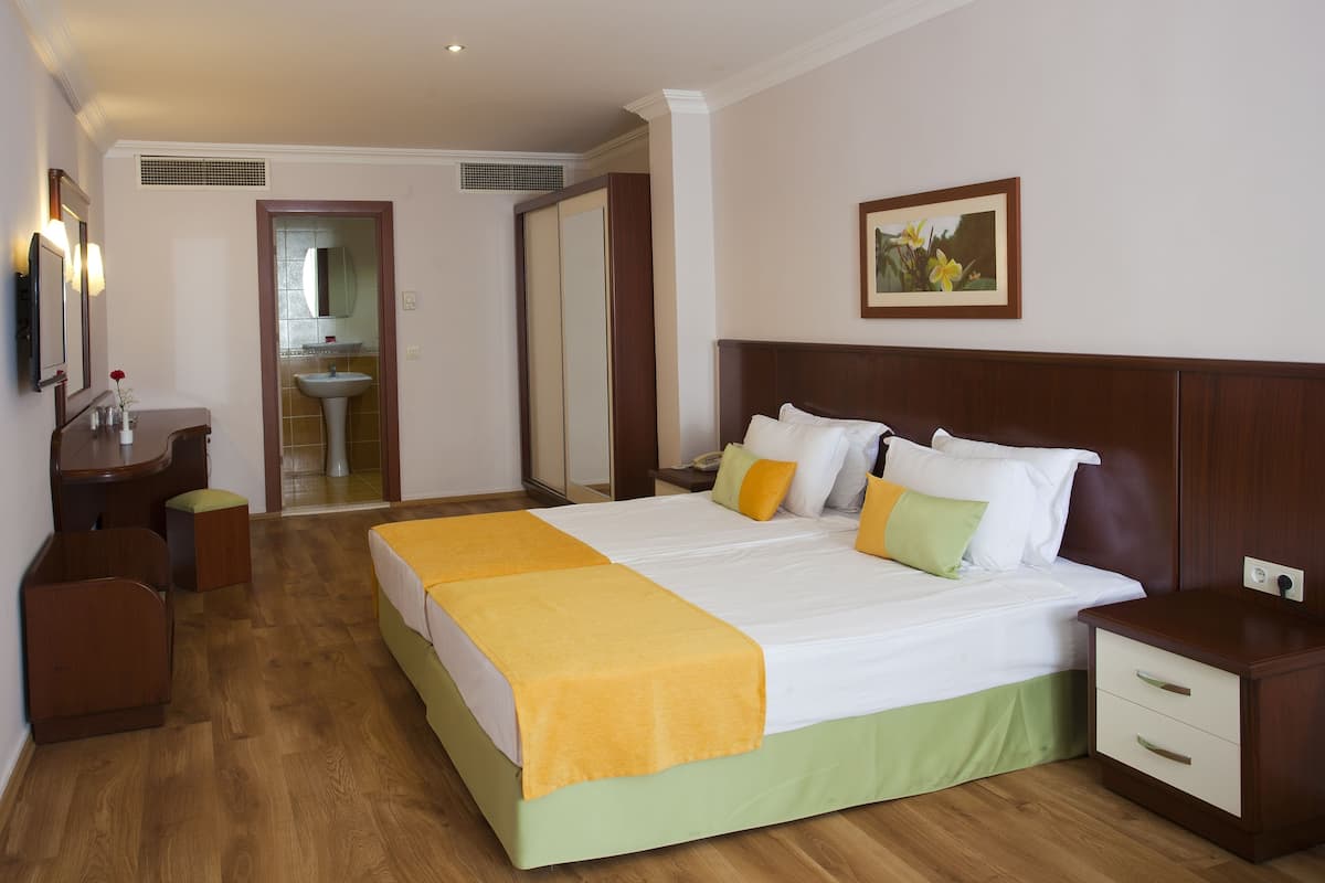 Habitación de hotel con una cama grande, mesitas de noche, un armario, baño con lavamanos y un cuadro en la pared.