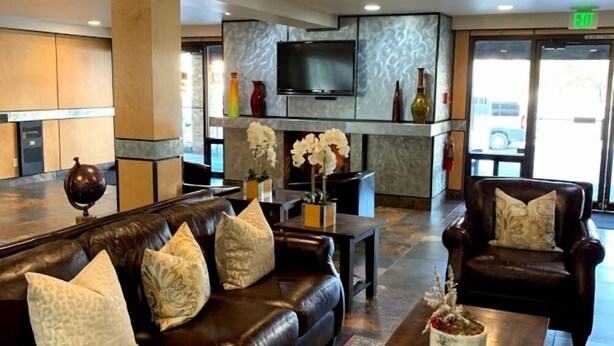 A lobby with a leather sofa, a wooden coffee table, and a television mounted on the wall.