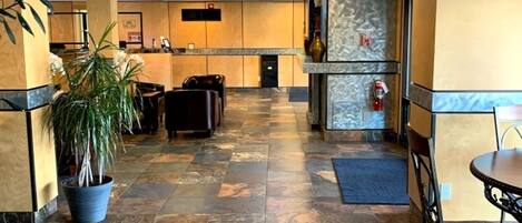 A hotel lobby with a reception desk, seating area, and a potted plant.