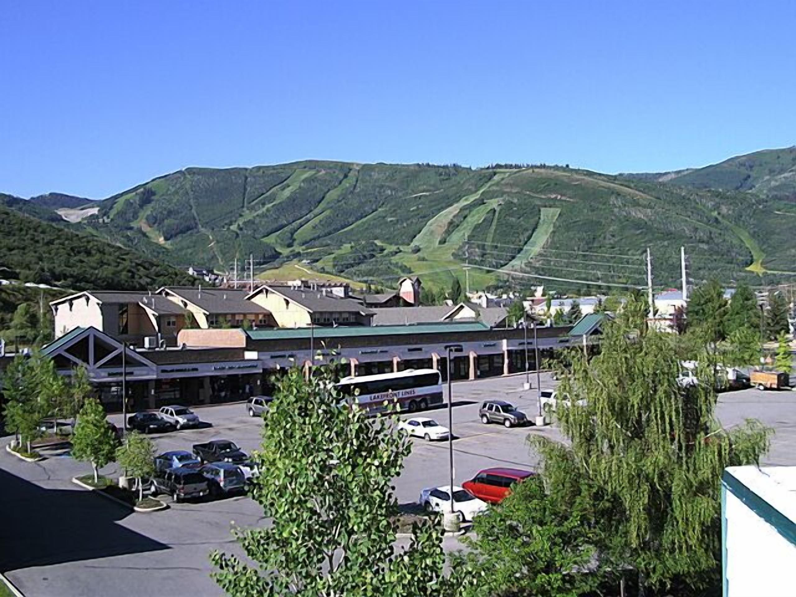 A parking lot with several cars, a building with a green roof, and a mountainous landscape in the background.