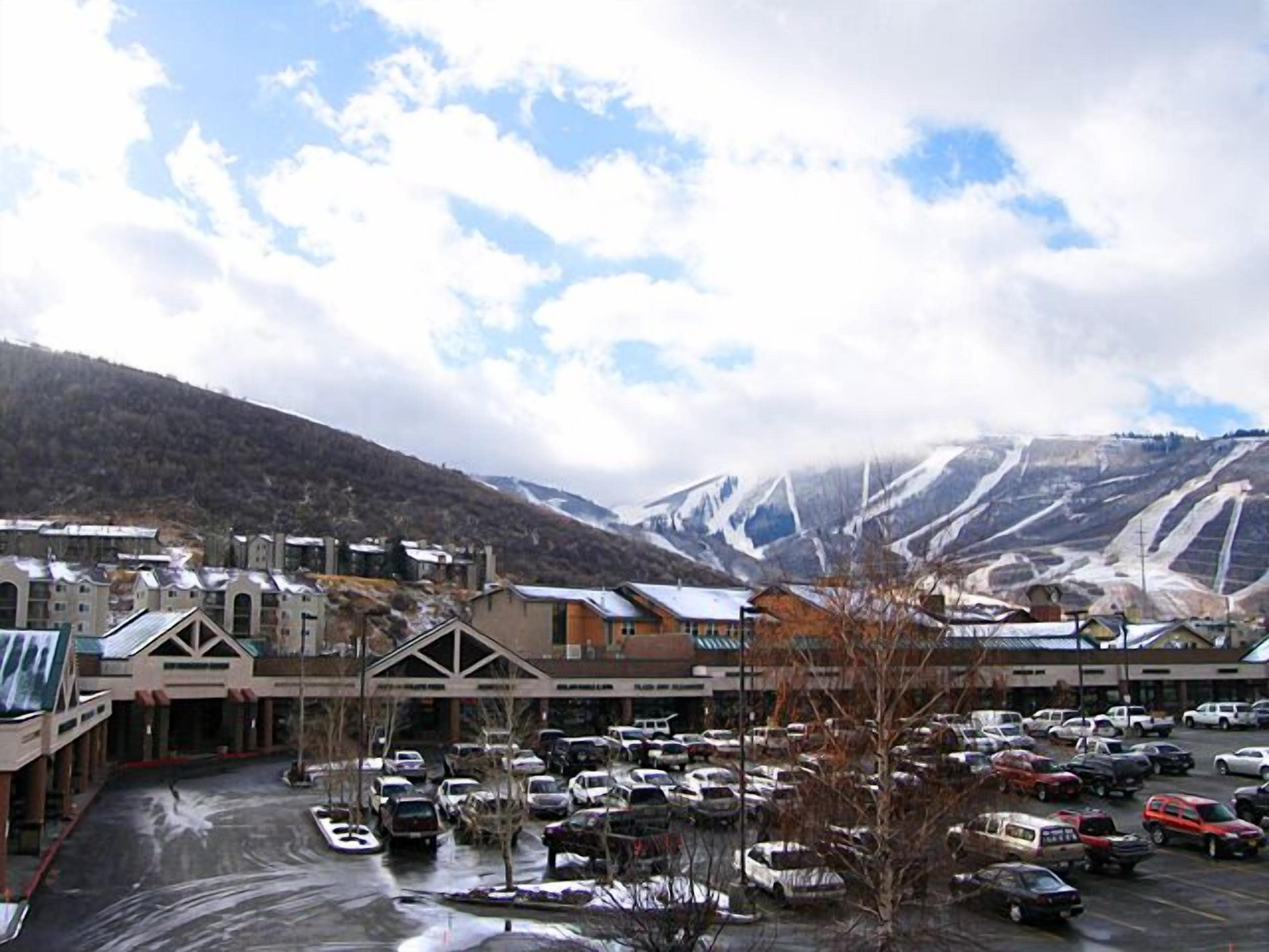 A parking lot with cars, buildings with sloped roofs, and a mountainous backdrop.