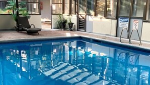A swimming pool with clear blue water, surrounded by a covered area with seating and potted plants.